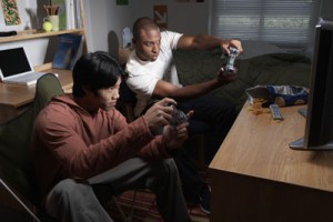 Two young men playing video game in dorm room, side view